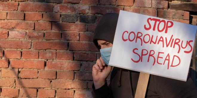 A man in a face mask carrying a sign that reads stop coronavirus spread.