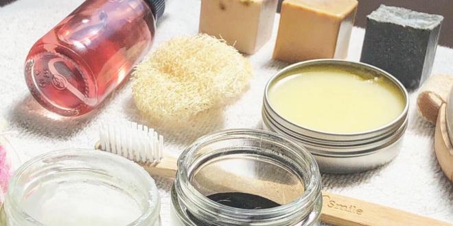 A variety of natural skin care products, soap bars, coconut oil, toner loofah, salves and more laid out on a whit towel.