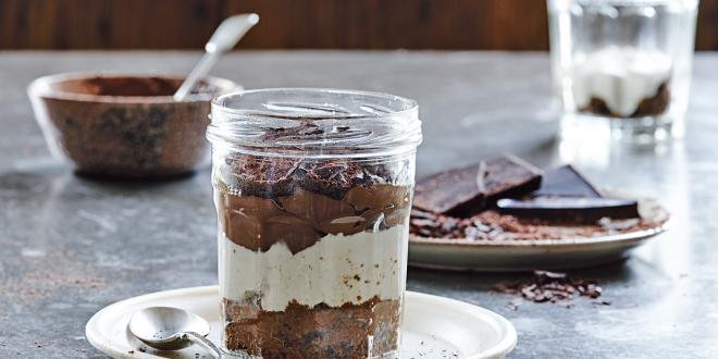 Tiramisu in a clear jar on a white plate with spoon. 