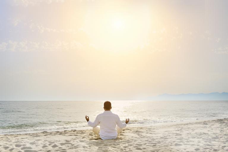 A man meditating on the beach facing a calm sea