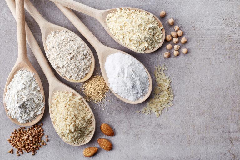 Wooden spoons of various gluten free flour on a light gray background.